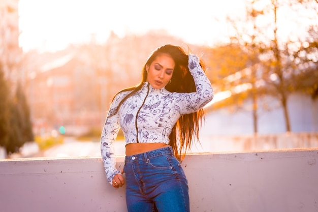 Una morena latina junto a una carretera en la ciudad junto a un árbol con flores rosas al atardecer