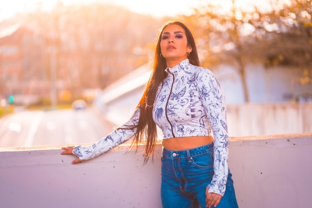 Una morena latina junto a una carretera en la ciudad junto a un árbol con flores rosas al atardecer