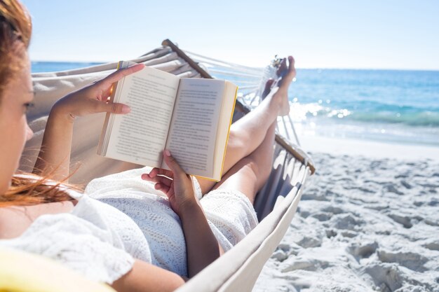 Morena lendo um livro enquanto relaxa na rede