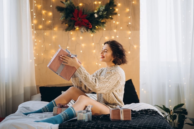 Morena linda e feliz na cama com caixas de presente ao redor