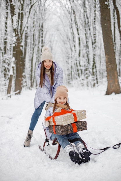 Morena madre y su hija montando un trineo en el bosque de invierno