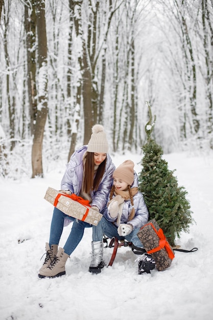 Morena madre y su hija montando un trineo en el bosque de invierno