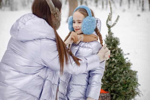 Morena madre y su hija de pie en el bosque de invierno