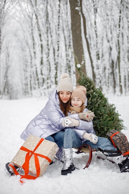 Morena madre y su hija sosteniendo una caja de regalo en el bosque de invierno