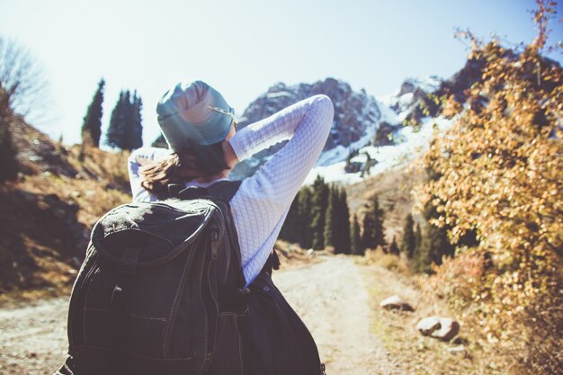 Una morena con mochila se estira al sol. Cielo despejado en las montañas.