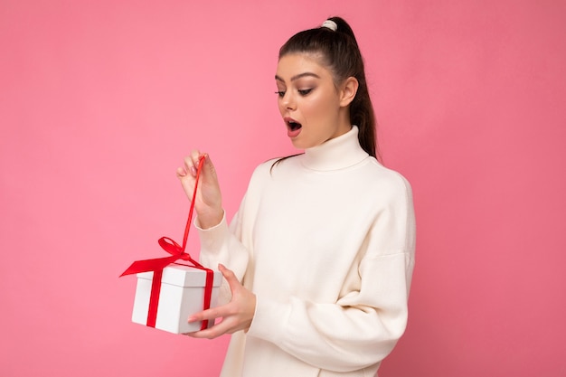 Morena mujer aislada sobre fondo colorido pared vistiendo ropa de moda look sosteniendo caja de regalo