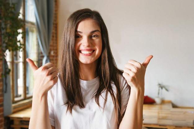 Morena mujer alegre de pelo largo mostrando grandes pulgares y sonriendo