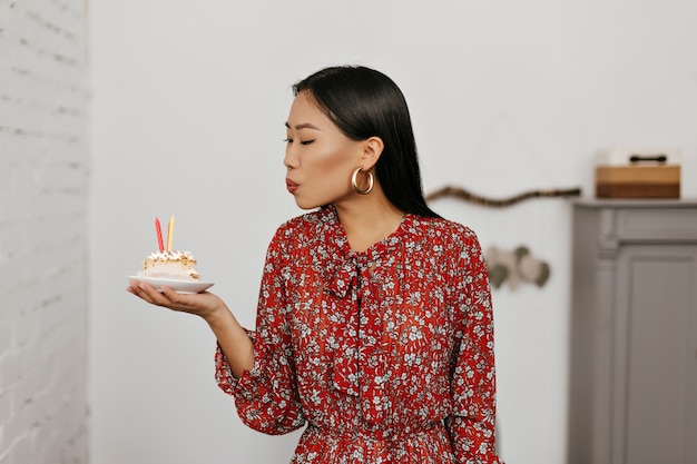 Morena mujer asiática sopla velas en la tarta de cumpleaños