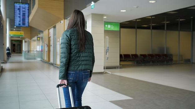 Morena mujer viajera está caminando en la terminal del aeropuerto moderno con maleta vista posterior El pasajero va a su vuelo en el aeropuerto de la ciudad