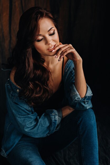 Una morena de pelo largo posa en un estudio sentada en el suelo sobre un fondo negro.