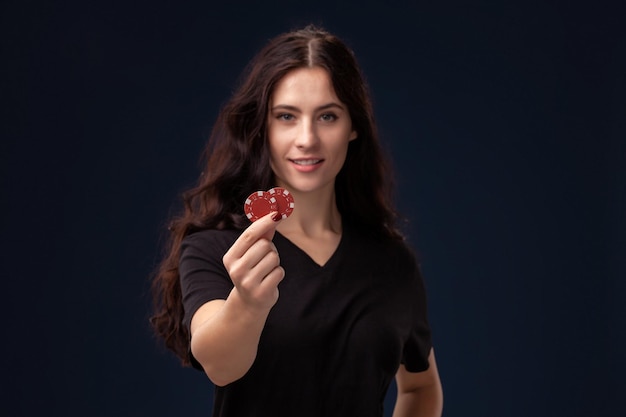 Morena de pelo rizado está posando con fichas de juego rojas en sus manos. Concepto de póquer sobre un fondo negro. Casino.