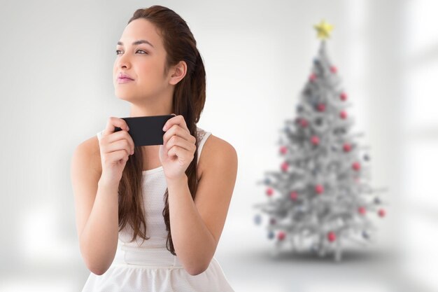 Morena pensativa sosteniendo su teléfono contra el árbol de navidad borroso en la habitación