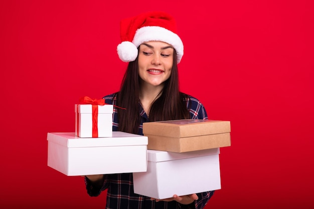 Una morena en pijama sostiene regalos de Navidad en cajas blancas sobre un fondo rojo Fotografía de estudio