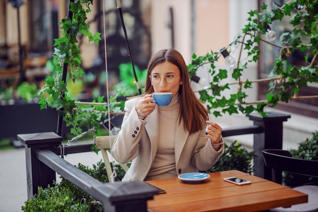 Morena sentada en la cafetería al aire libre y bebiendo su espresso