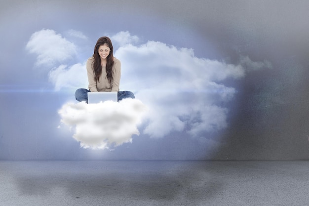 Morena sentada en la nube usando una computadora portátil contra las nubes en una habitación
