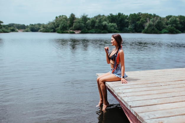 Morena sexy e linda se bronzear na ponte perto do lago ou rio em um maiô preto. conceito de turismo e lazer.