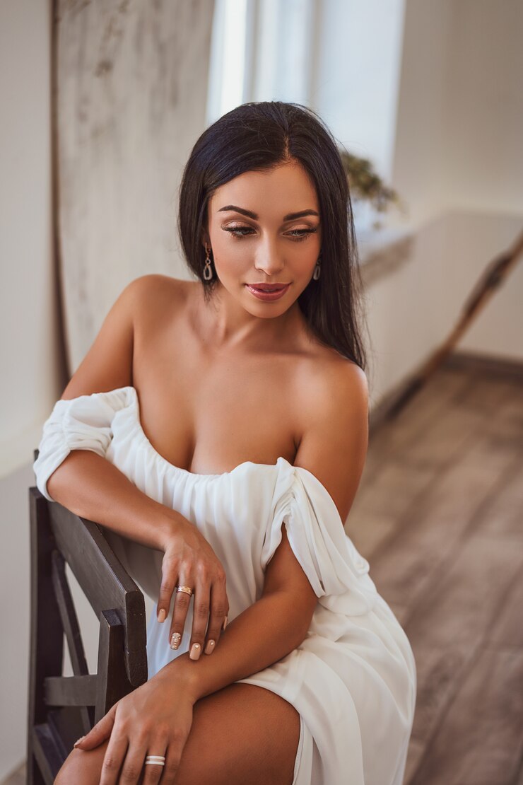 Foto morena sexy sentada em um vestido branco pela janela