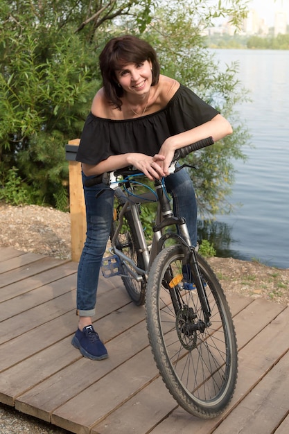 Foto la morena sonriente se detuvo a descansar en la orilla del río mientras conducía una bicicleta