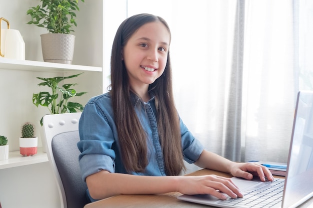 Morena sonriente estudiando en la computadora en casa aprendiendo a hacer la tarea mirando a la cámara