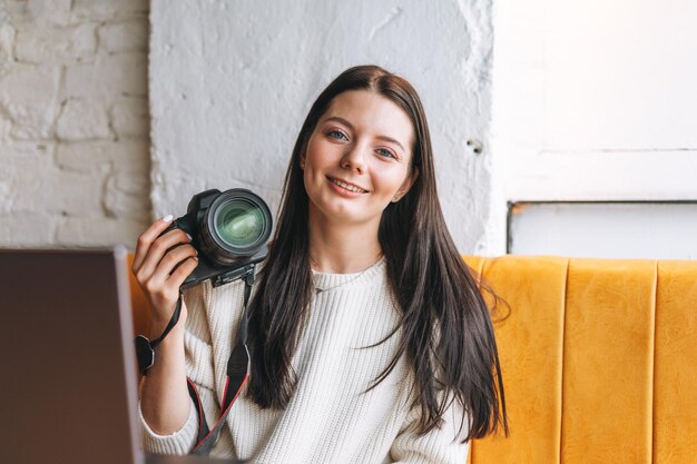 Morena sonriente joven fotógrafa trabajando con su cámara y portátil en el café