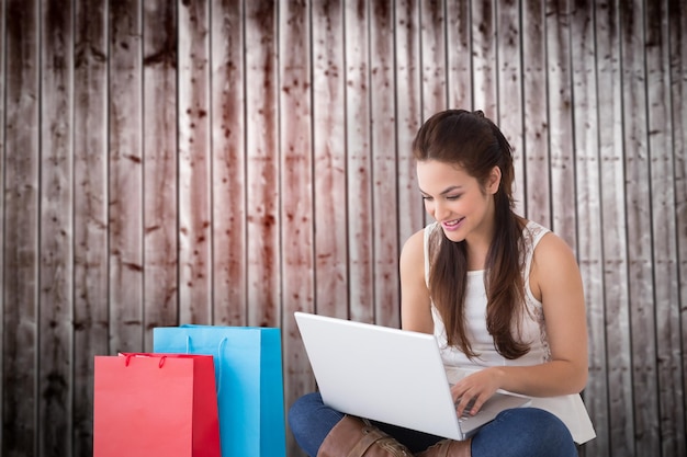 Foto morena sonriente sentada y usando su computadora portátil contra tablones de madera