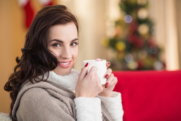 Morena sonriente sosteniendo una taza de chocolate caliente en Navidad