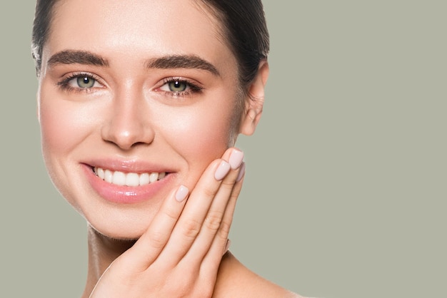 Morena sorridente natural maquiagem cosméticos de beleza de mulher tocando seu rosto. Cor de fundo. Verde