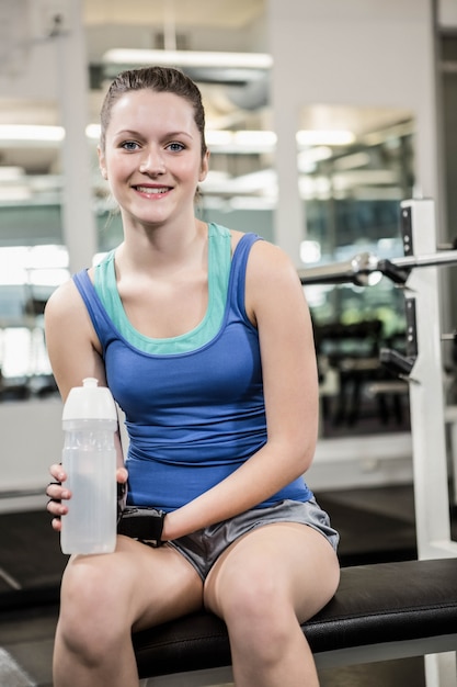 Morena sorridente no banco segurando a garrafa de água no ginásio