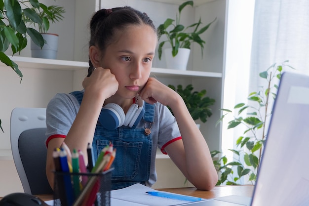 Foto morena triste de 11 a 13 años se sienta en casa con una computadora, hace la tarea, se comunica en internet.