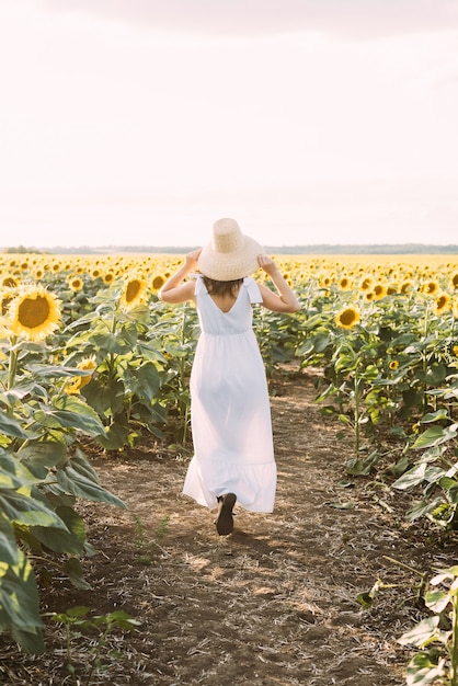 Morena woma em uma roupa de verão elegante e chapéu de palha sob os raios do sol na caminhada pela natureza