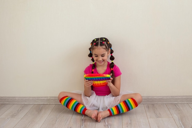 Foto moreninha sorridente em roupas multicoloridas brilhantes e meias arco-íris se senta no chão contra um ...