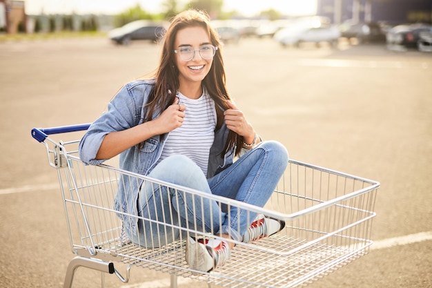 Morenita joven que se sienta en la carretilla de compras