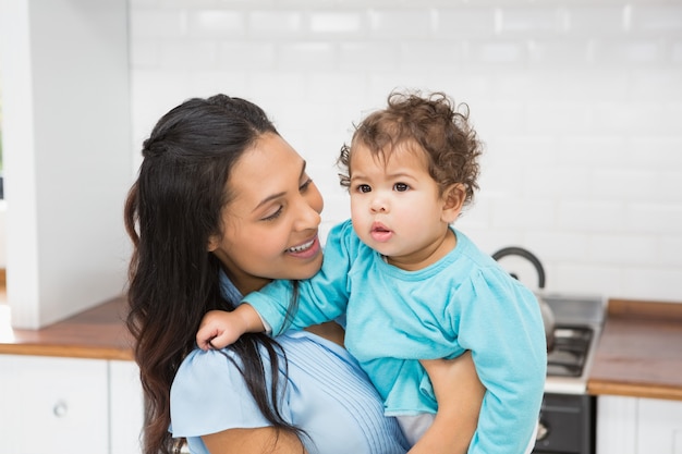 Morenita sonriente que detiene a su bebé en la cocina