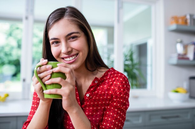 Morenita sonriente que sostiene la taza en la cocina