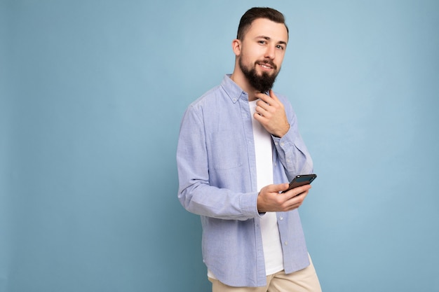 Moreno bonito e jovem com barba por fazer e barba, vestindo uma camiseta branca elegante e uma camisa azul isolada