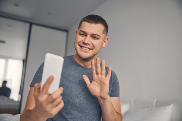 Moreno bonito em um ambiente confortável e parecendo animado enquanto fala no celular e acena