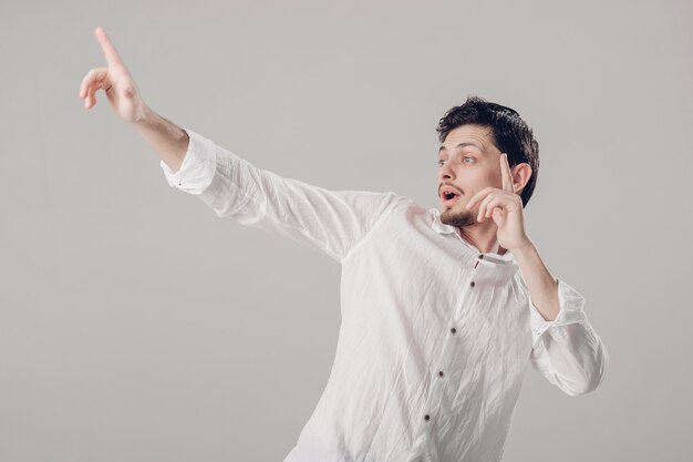 Moreno jovem bonito com uma camisa branca, dançando e se divertindo no fundo cinza. luz suave