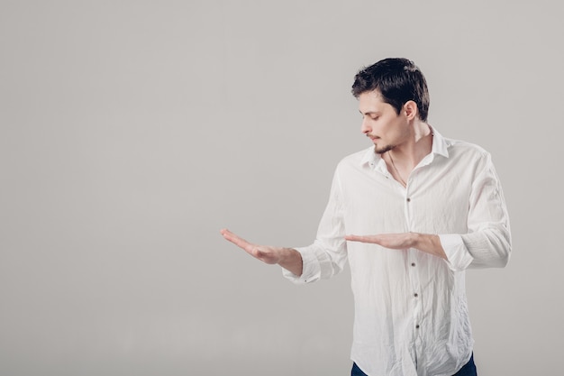 Moreno jovem bonito com uma camisa branca, dançando e se divertindo no fundo cinza. luz suave