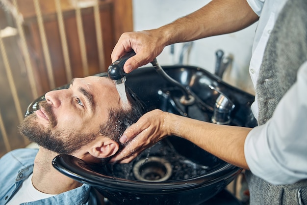 Moreno relaxado com a cabeça na pia para lavar o cabelo de uma barbearia