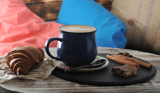 Morgen-Frühstück am Cafécappuccino in einem Becher mit Milchschaum und einem Hörnchen