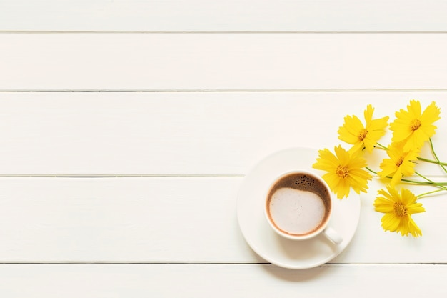 Morgen Tasse frischen Kaffee Cappuccino mit frühlingsgelben Blumen auf einem weißen Holztisch.