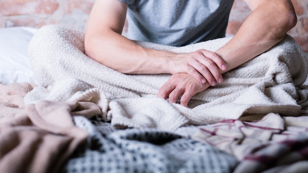 Morgen wieder. Zeit aufzuwachen. Mann sitzt im unordentlichen Bett. Hände gefaltet. Stress und Schlaflosigkeit.