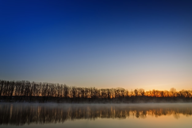 Morgendämmerung über der glatten Oberfläche des Frühlingsflusses.