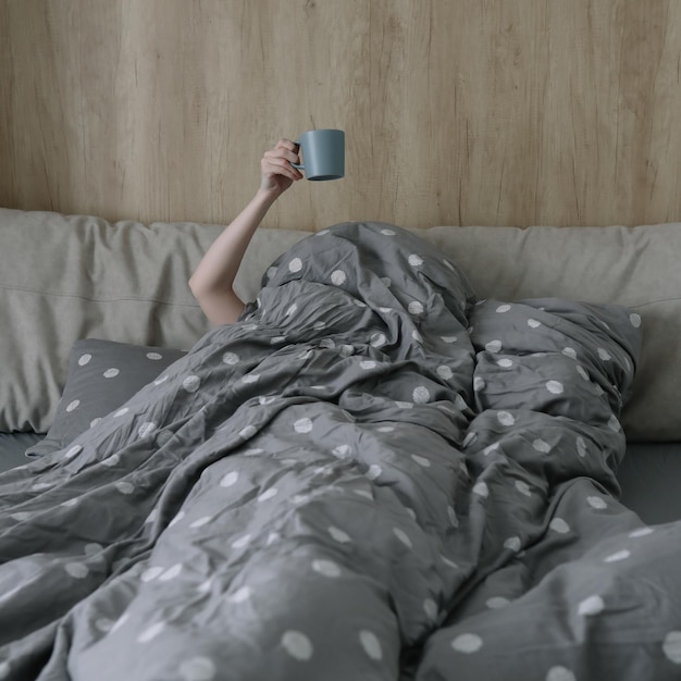 Morgendliche Gemütlichkeit gemütliches Wohnkonzept eine Hand mit einer Tasse Kaffee oder Tee im Bett zu Hause