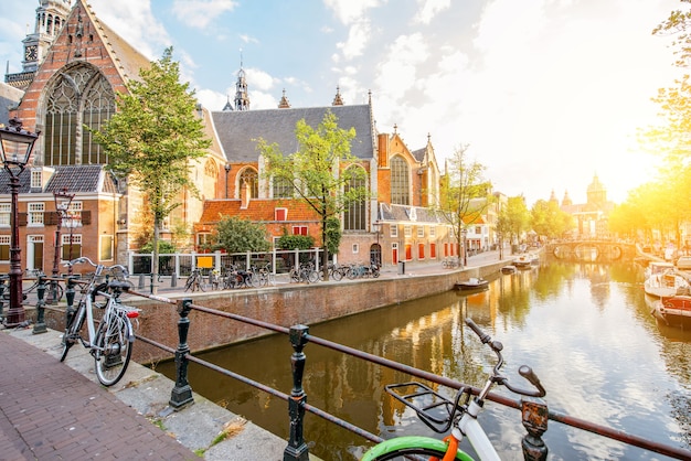 Morgendlicher Blick auf den Wasserkanal mit alter Kirche während des sonnigen Wetters in Amsterdam-Stadt