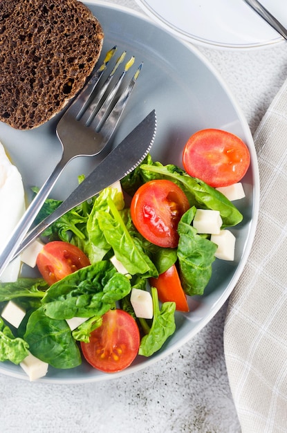 Morgenfrühlingstischdekoration. Salat in Teller, Ei, Tasse Kaffee und Croissant, frische Tulpen in Vase auf sauberem weißem Tischtuchhintergrund. Frühstückstisch Gedeck in weißer Farbe.