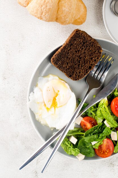 Morgenfrühlingstischdekoration. Salat in Teller, Ei, Tasse Kaffee und Croissant, frische Tulpen in Vase auf sauberem weißem Tischtuchhintergrund. Frühstückstisch Gedeck in weißer Farbe.