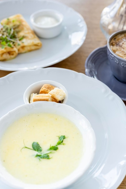 Morgenfrühstück mit Käsesuppe, Kaffeecroutons, Pfannkuchen und Gemüse vor dem Hintergrund von Bac