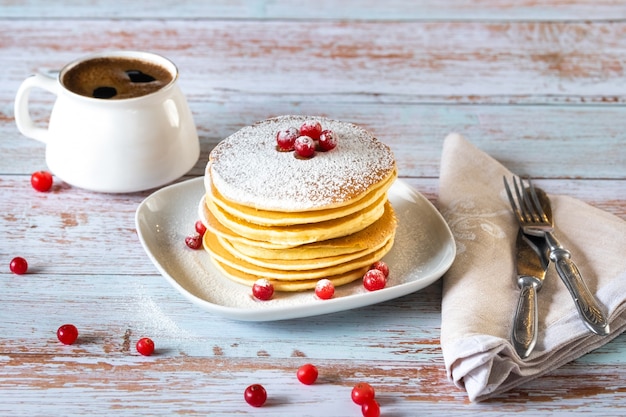 Morgenfrühstück mit Pfannkuchen mit Preiselbeeren und Puderzucker und einer Tasse Kaffee auf einem Holztisch.