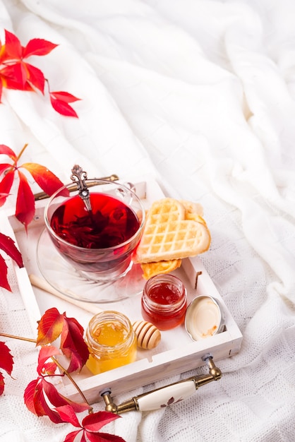 Morgenfrühstück mit rotem Tee, Honig und Waffeln auf einem Bett